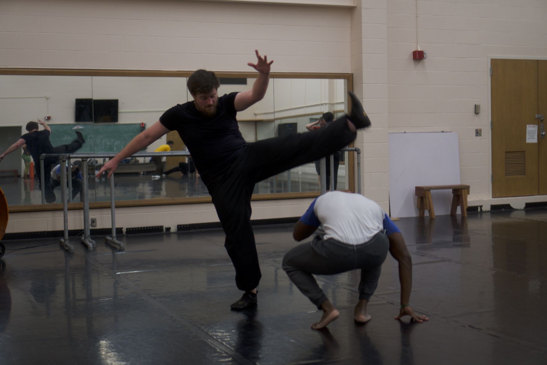 A man kicks his foot high in the air as another man dodges it by crouching to the ground